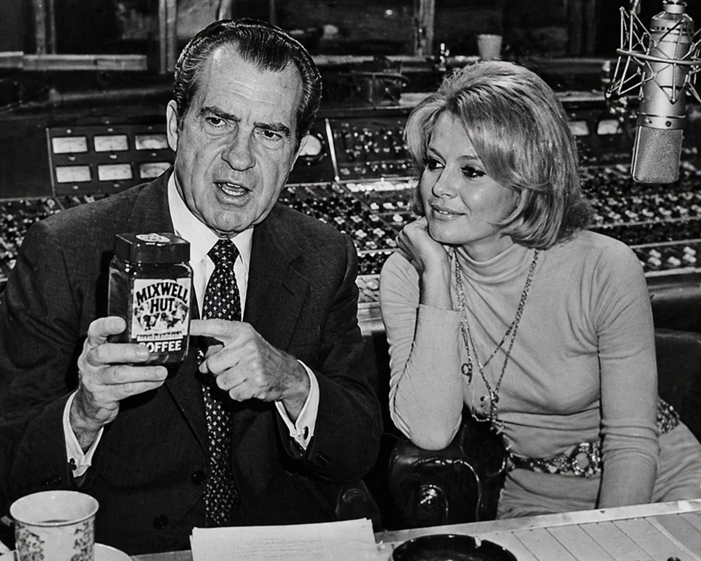Richard Nixon in a recording studio holds a jar labeled Mixwell Hut Coffee while a woman resembling a 1970s television actress watches beside him.